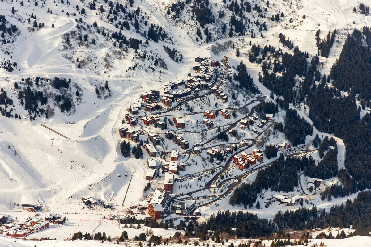 Val Thorens chalets in a snowy high bowl, seen from a piste with a chairlift and skiers in the foreground